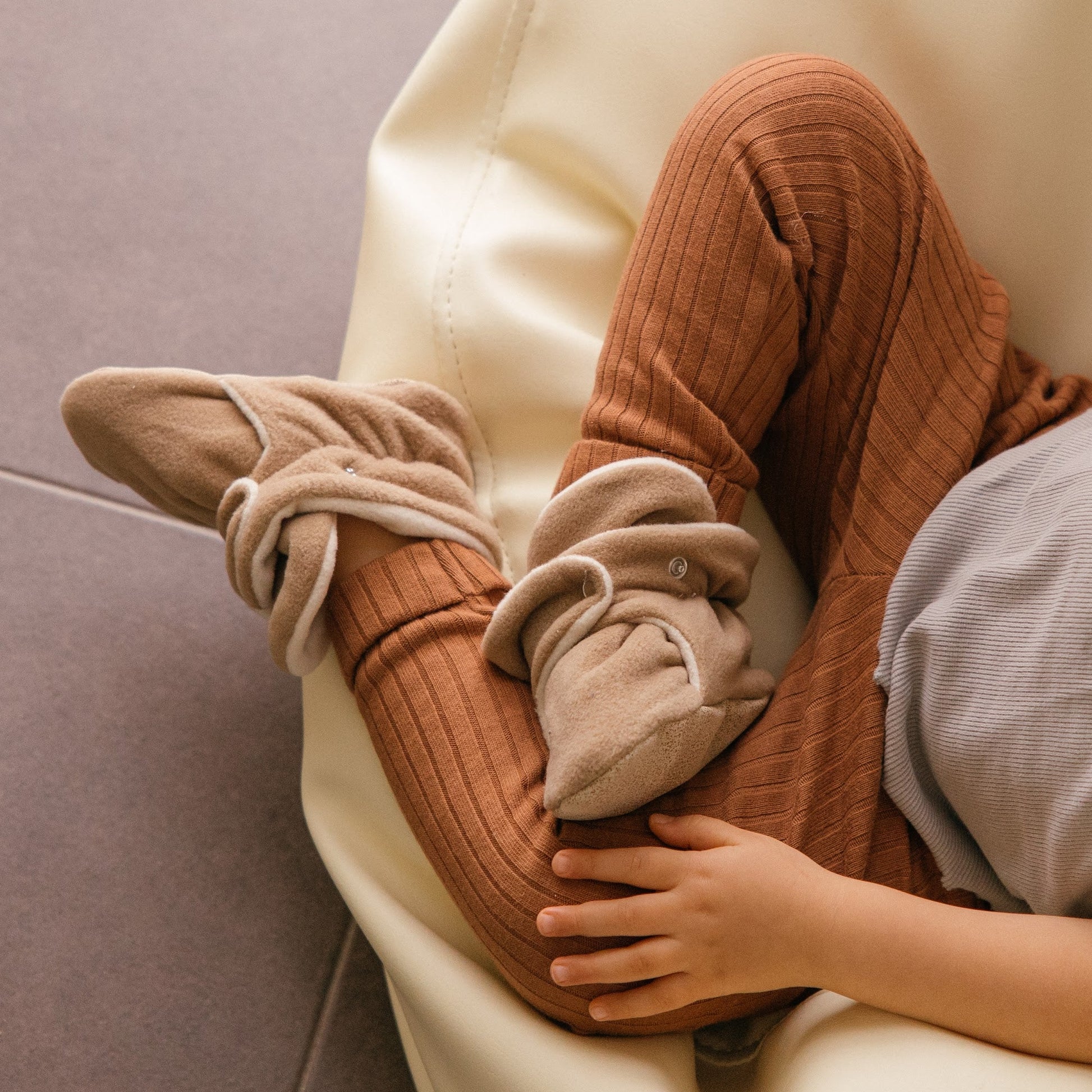 Chaussons en polaire brun latte aux pieds d’un tout-petit.