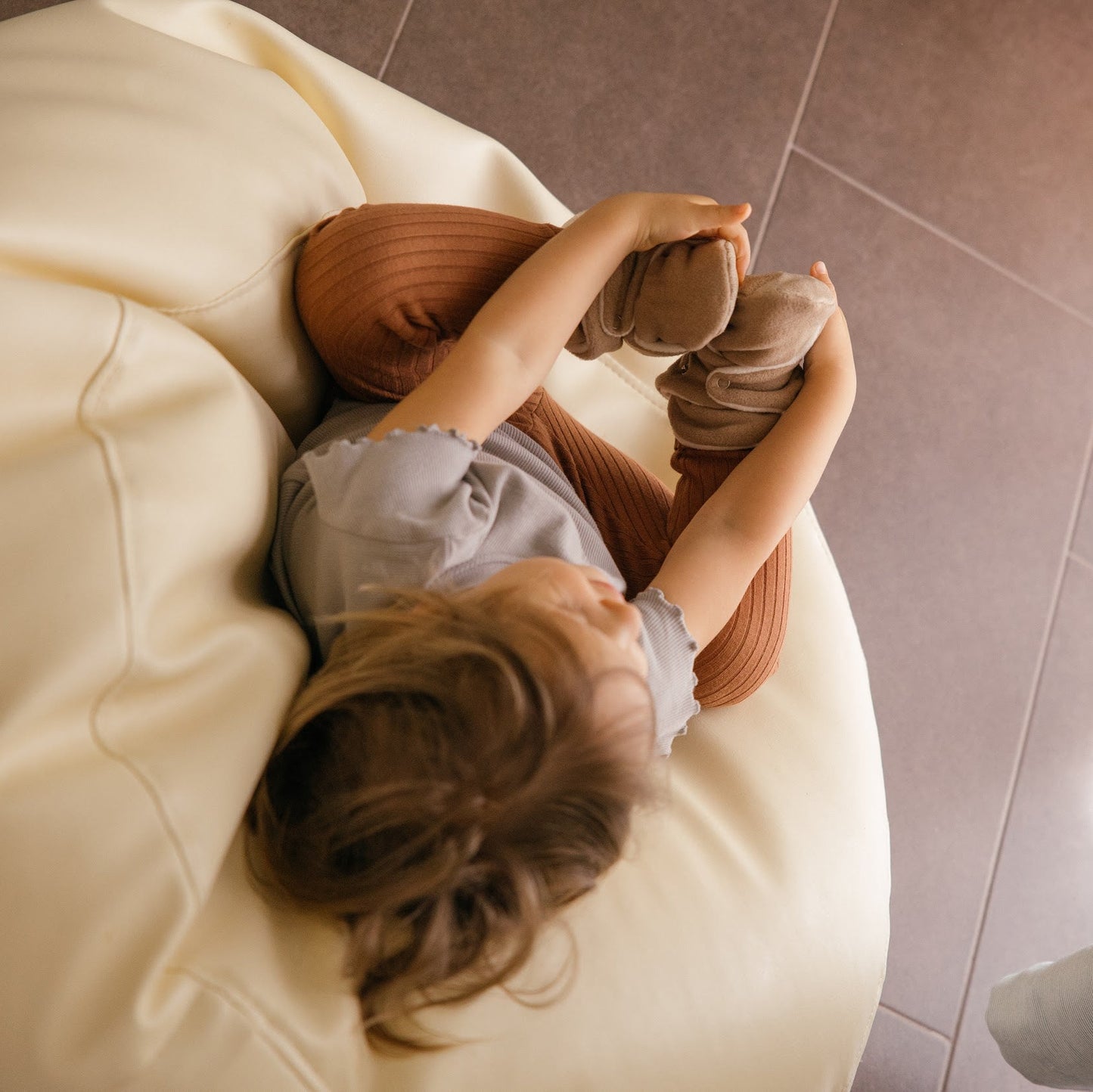 Chaussons en polaire brun latte aux pieds d’un tout-petit.