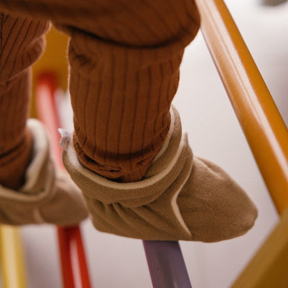 Chaussons en polaire brun latte aux pieds d’un tout-petit.
