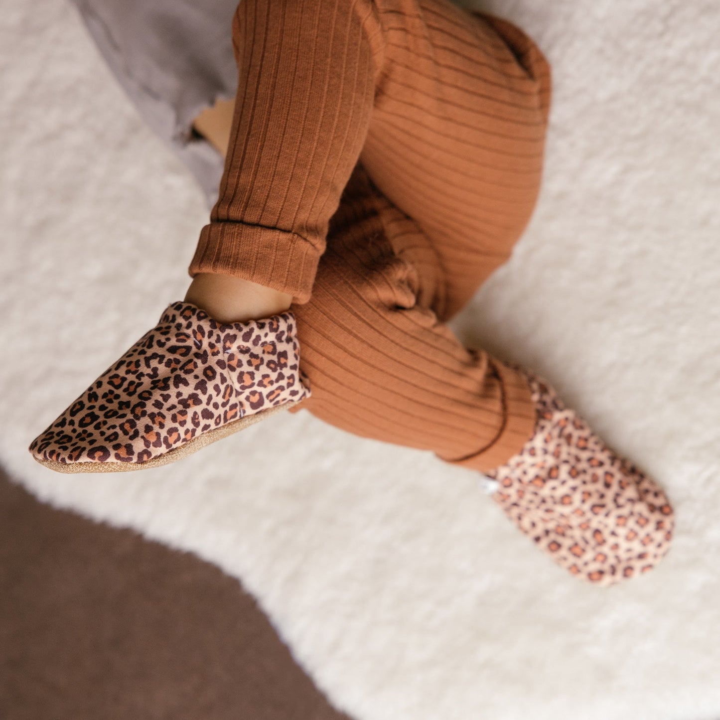 Bébé portant des chaussons à imprimé léopard assis sur une couverture douillette.