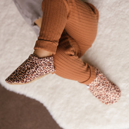 Bébé portant des chaussons à imprimé léopard assis sur une couverture douillette.