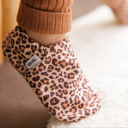 Bébé portant des chaussons à imprimé léopard assis sur une couverture douillette.