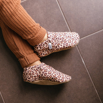 Bébé portant des chaussons à imprimé léopard assis sur une couverture douillette.