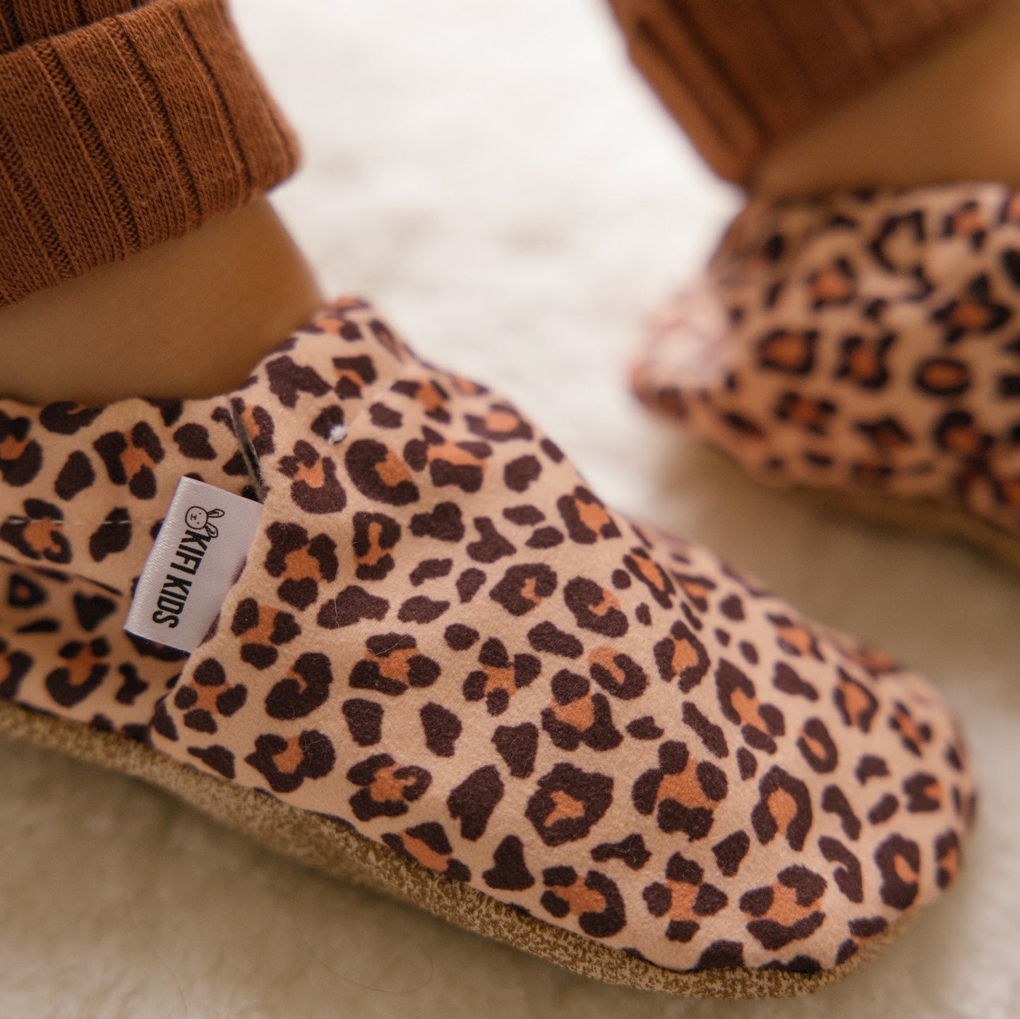 Bébé portant des chaussons à imprimé léopard assis sur une couverture douillette.