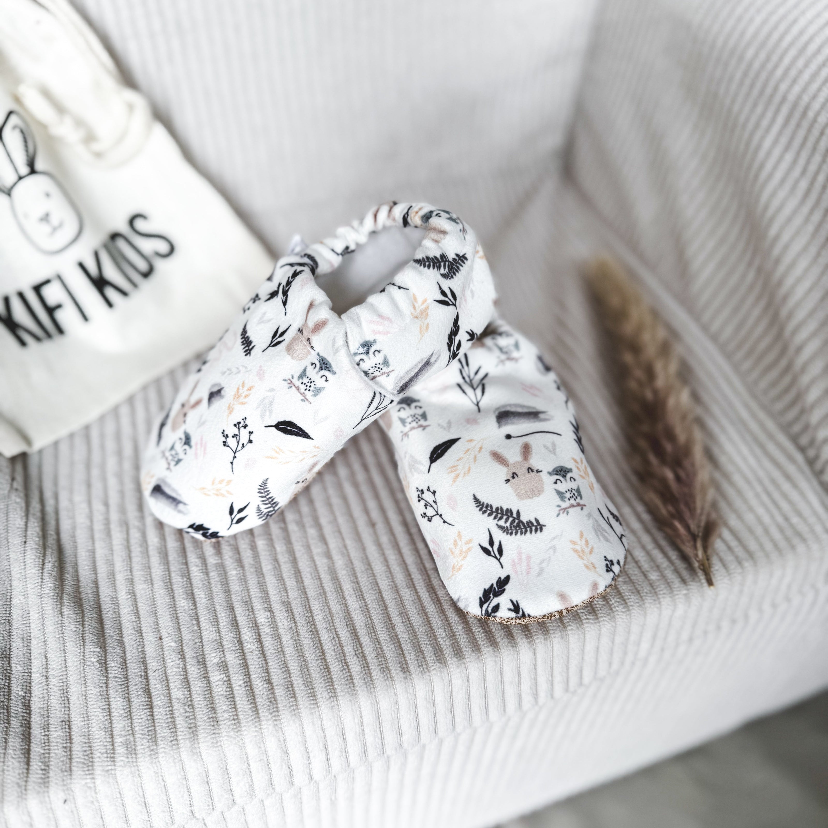 Rabbit baby shoes on a baby chair with a white bag labeled 'KifiKids' in the background.