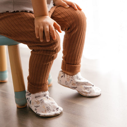 Bébé portant des chaussons à imprimé lapin tout doux, assis sur une chaise.