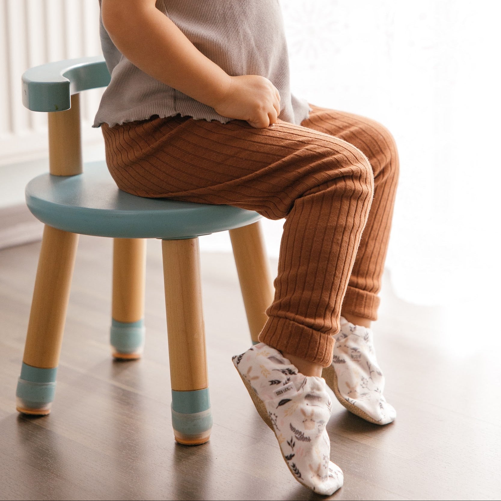 Bébé portant des chaussons à imprimé lapin tout doux, assis sur une chaise.
