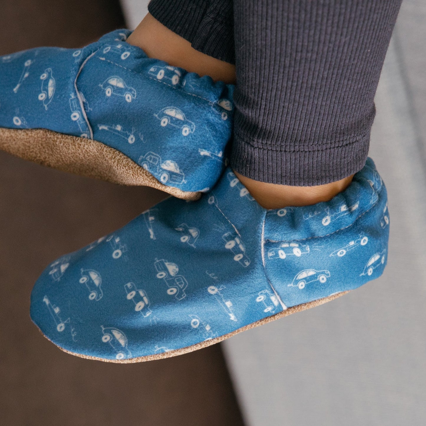 Chaussons pour bébé souples avec un motif amusant de voitures de course sur un tissu bleu marine, parfaits pour les tout-petits et les petits garçons.