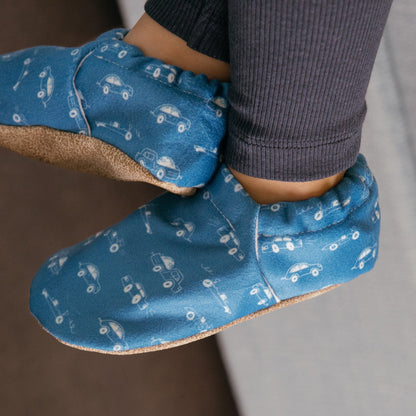 Chaussons pour bébé souples avec un motif amusant de voitures de course sur un tissu bleu marine, parfaits pour les tout-petits et les petits garçons.