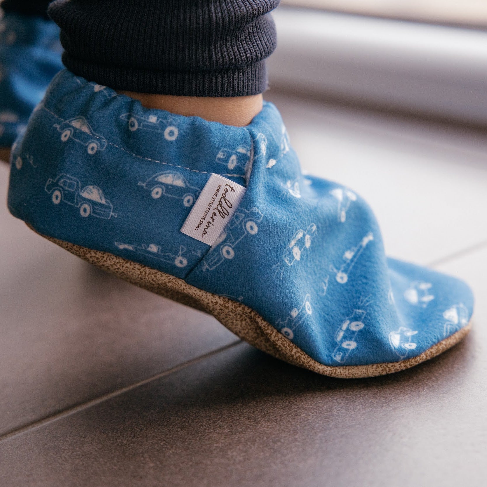 Chaussons pour bébé souples avec un motif amusant de voitures de course sur un tissu bleu marine, parfaits pour les tout-petits et les petits garçons.