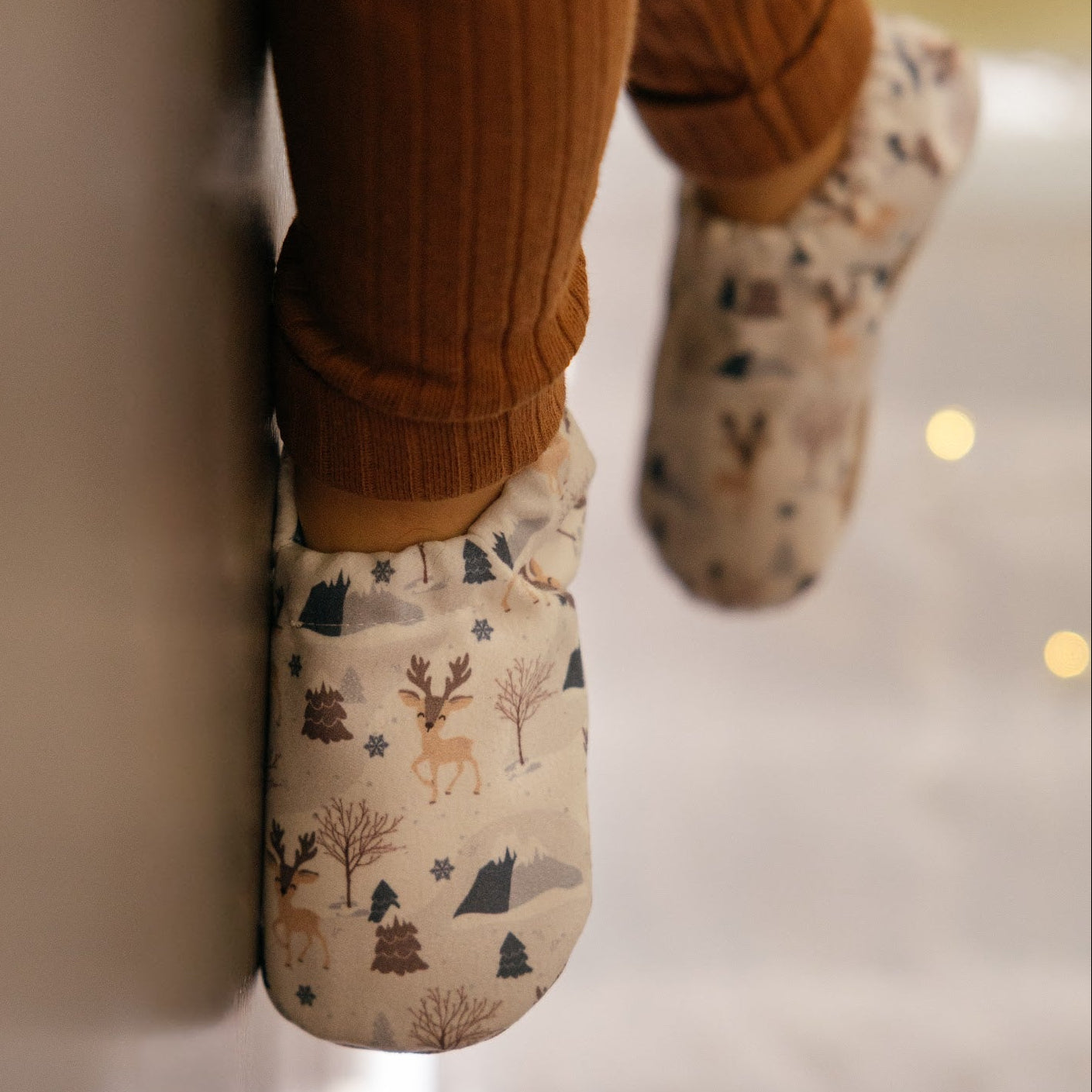 Chaussons pour bébé souples avec un motif hivernal chaleureux de rennes, flocons de neige et montagnes, parfaits pour la période des fêtes.