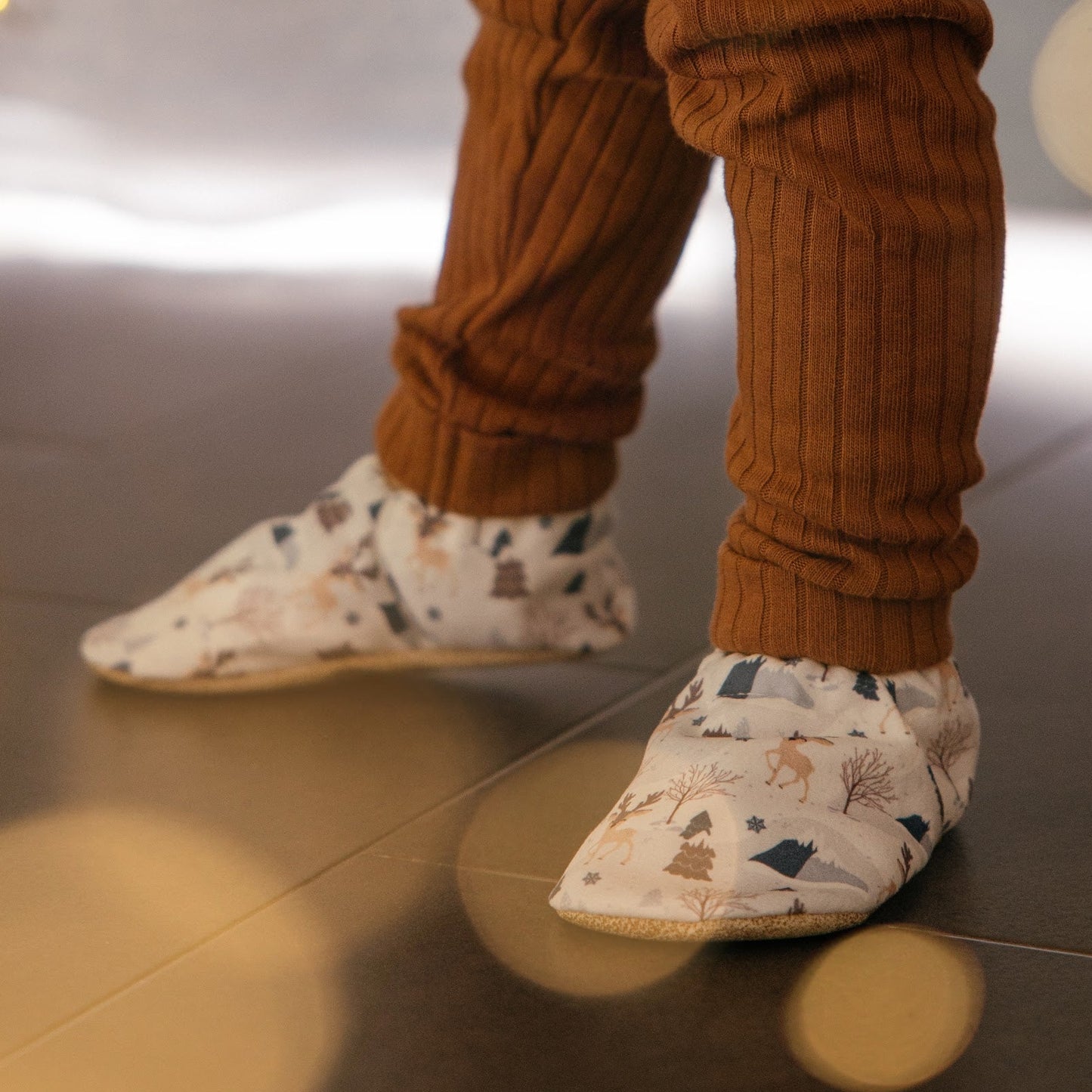 Chaussons pour bébé souples avec un motif hivernal chaleureux de rennes, flocons de neige et montagnes, parfaits pour la période des fêtes.
