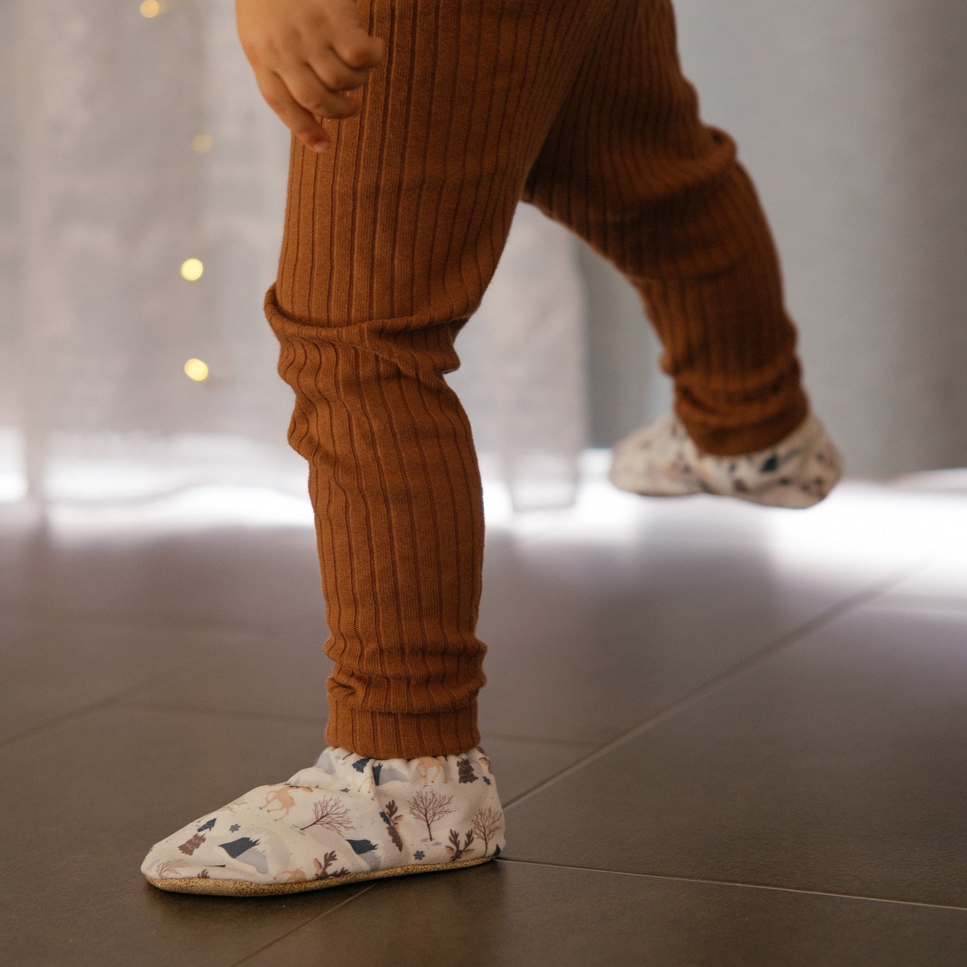 Chaussons pour bébé souples avec un motif hivernal chaleureux de rennes, flocons de neige et montagnes, parfaits pour la période des fêtes.