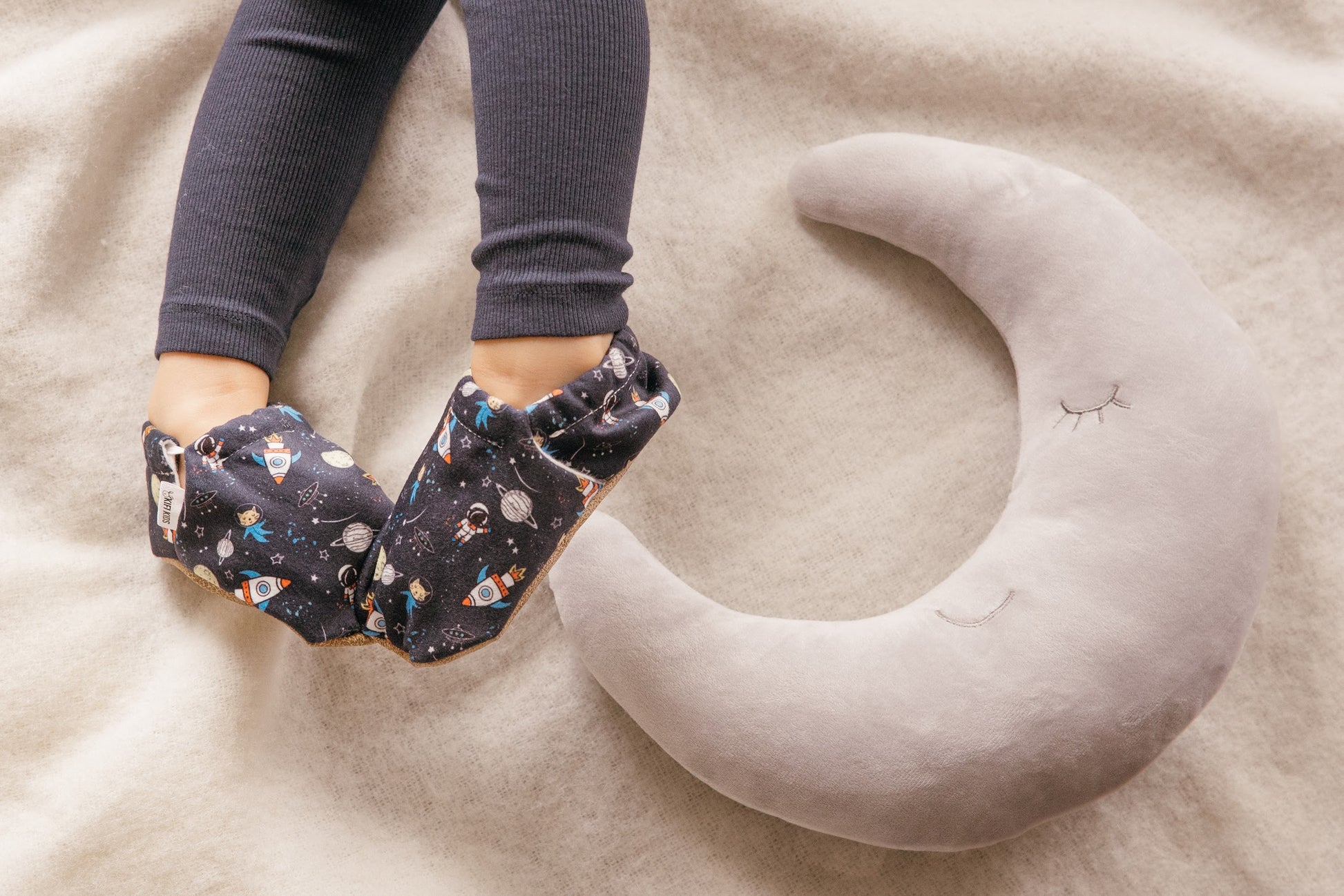 Chaussons d’intérieur pour enfant à motif espace avec fusées et étoiles, portés par un enfant