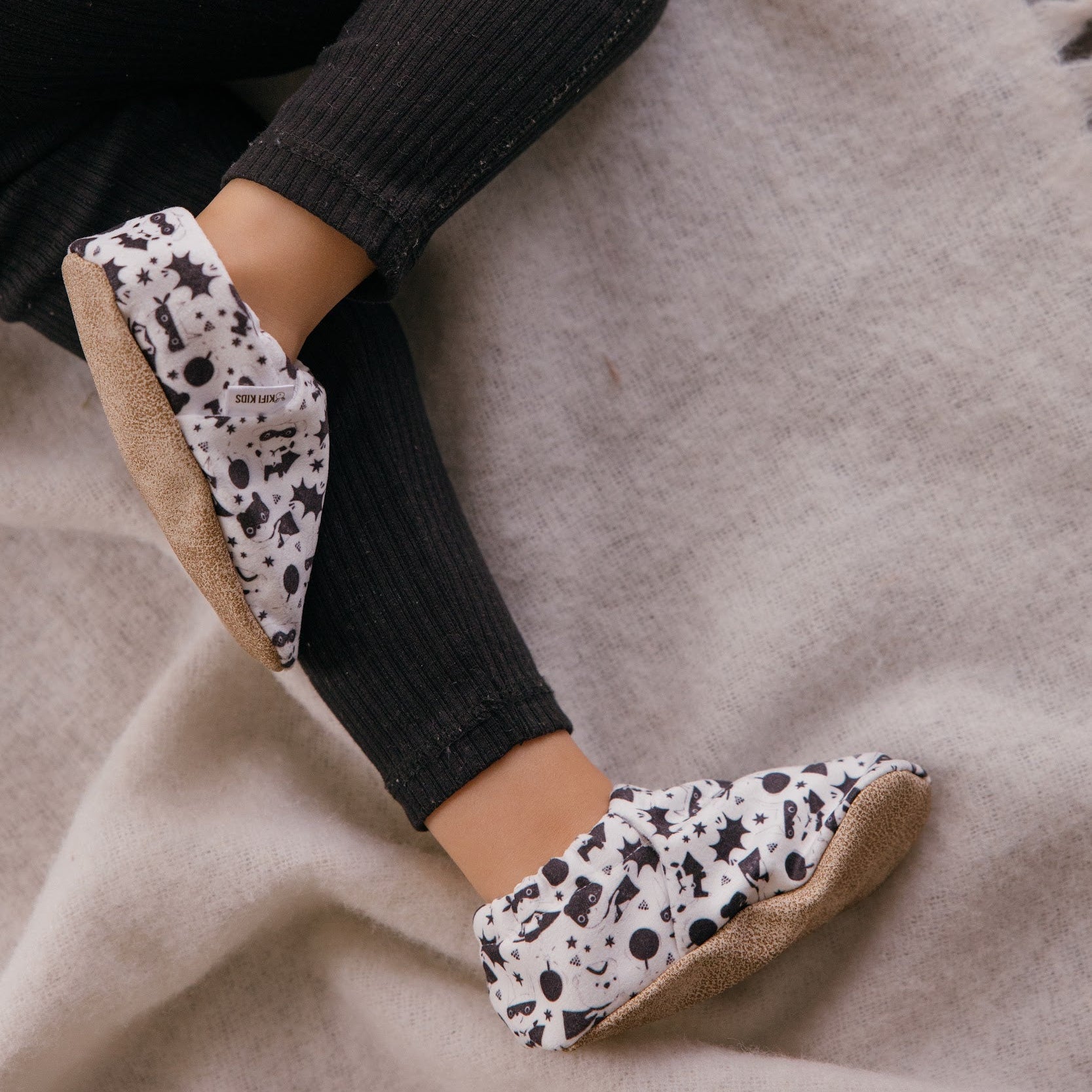 Chaussons bébé avec des animaux vêtus de costumes de super-héros sur un fond blanc.