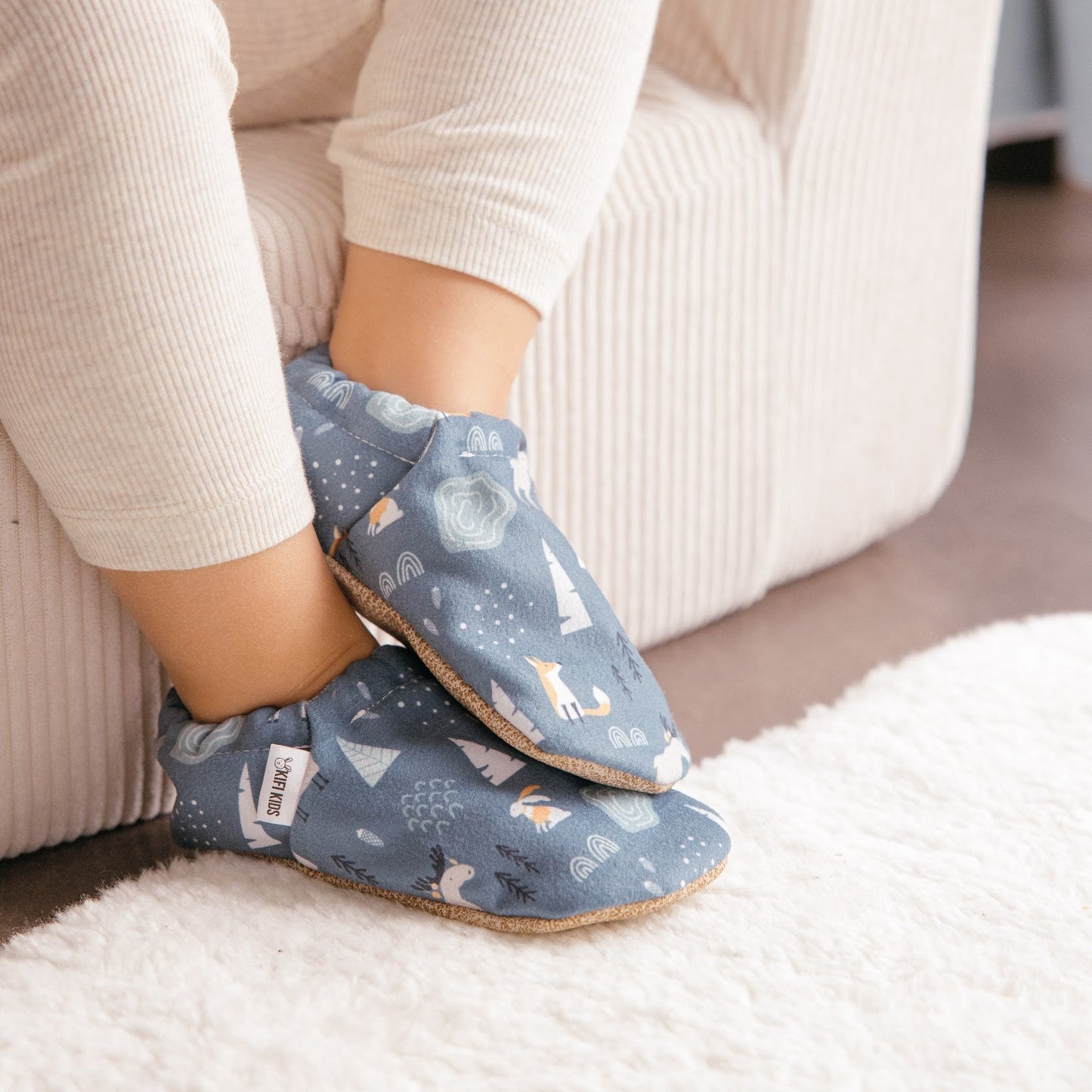 Chaussons bébé avec motif d’animaux d’hiver représentant des lapins, des renards et des élans sur un fond bleu doux.