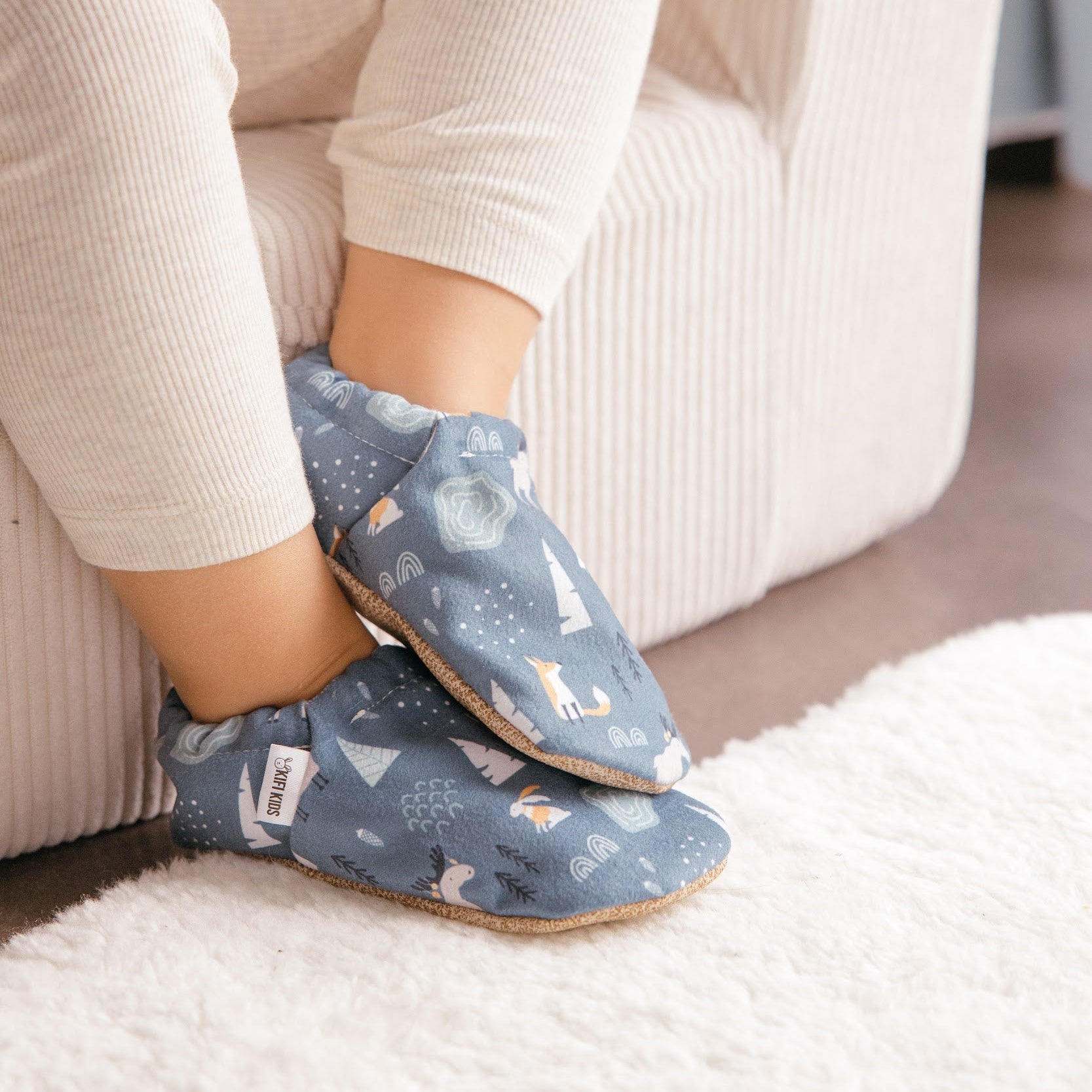 Chaussons bébé avec motif d’animaux d’hiver représentant des lapins, des renards et des élans sur un fond bleu doux.