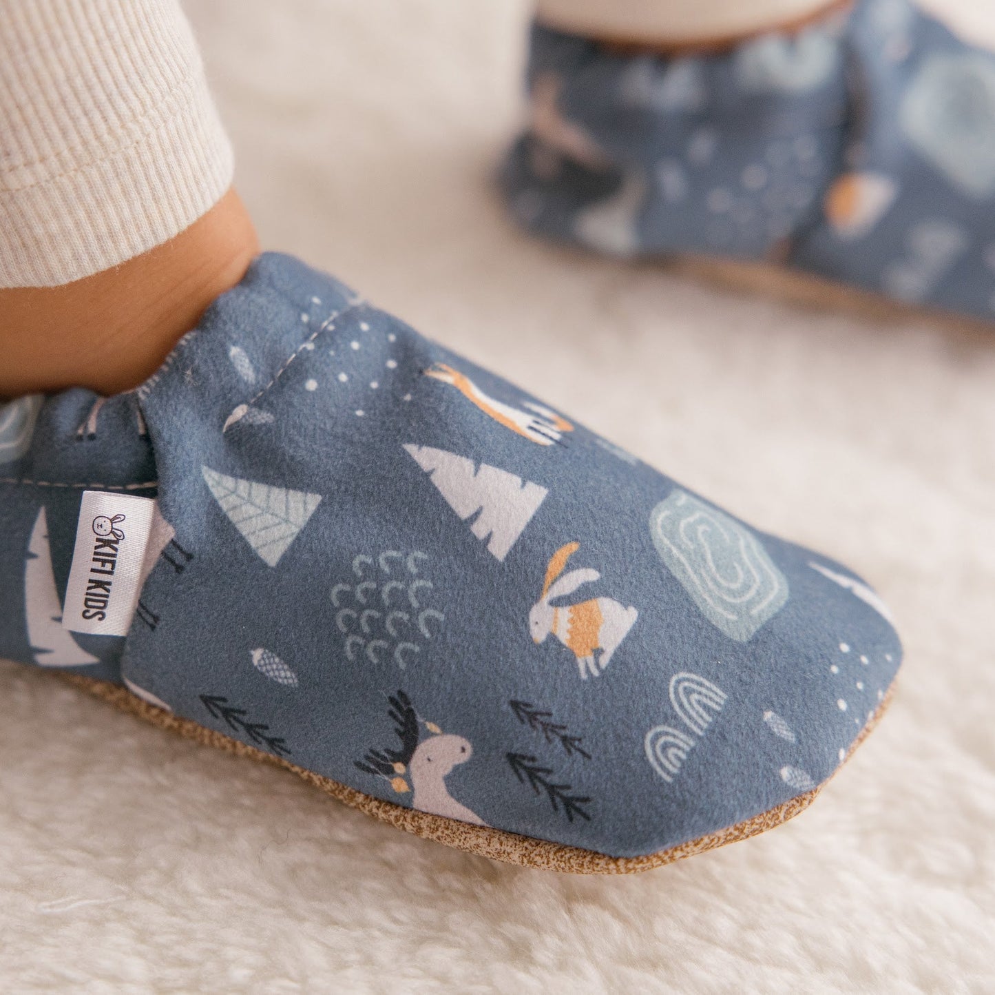Chaussons bébé avec motif d’animaux d’hiver représentant des lapins, des renards et des élans sur un fond bleu doux.