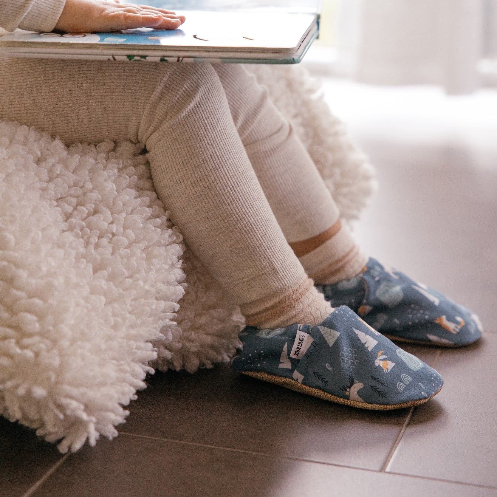 Chaussons bébé avec motif d’animaux d’hiver représentant des lapins, des renards et des élans sur un fond bleu doux.