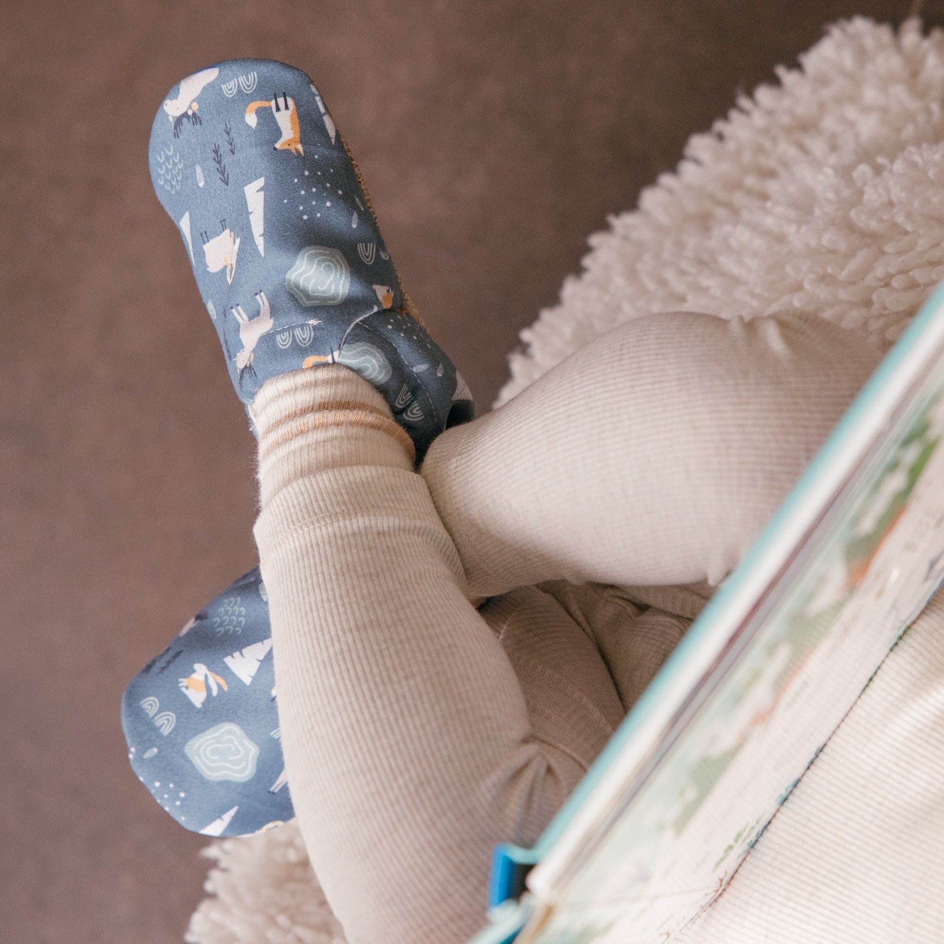 Chaussons bébé avec motif d’animaux d’hiver représentant des lapins, des renards et des élans sur un fond bleu doux.